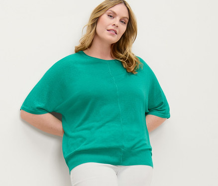 Frau posiert an einer Wand, trägt ein Feinstrick-Shirt mit Leinen und eine 7/8-Treggings mit Lochstickerei.