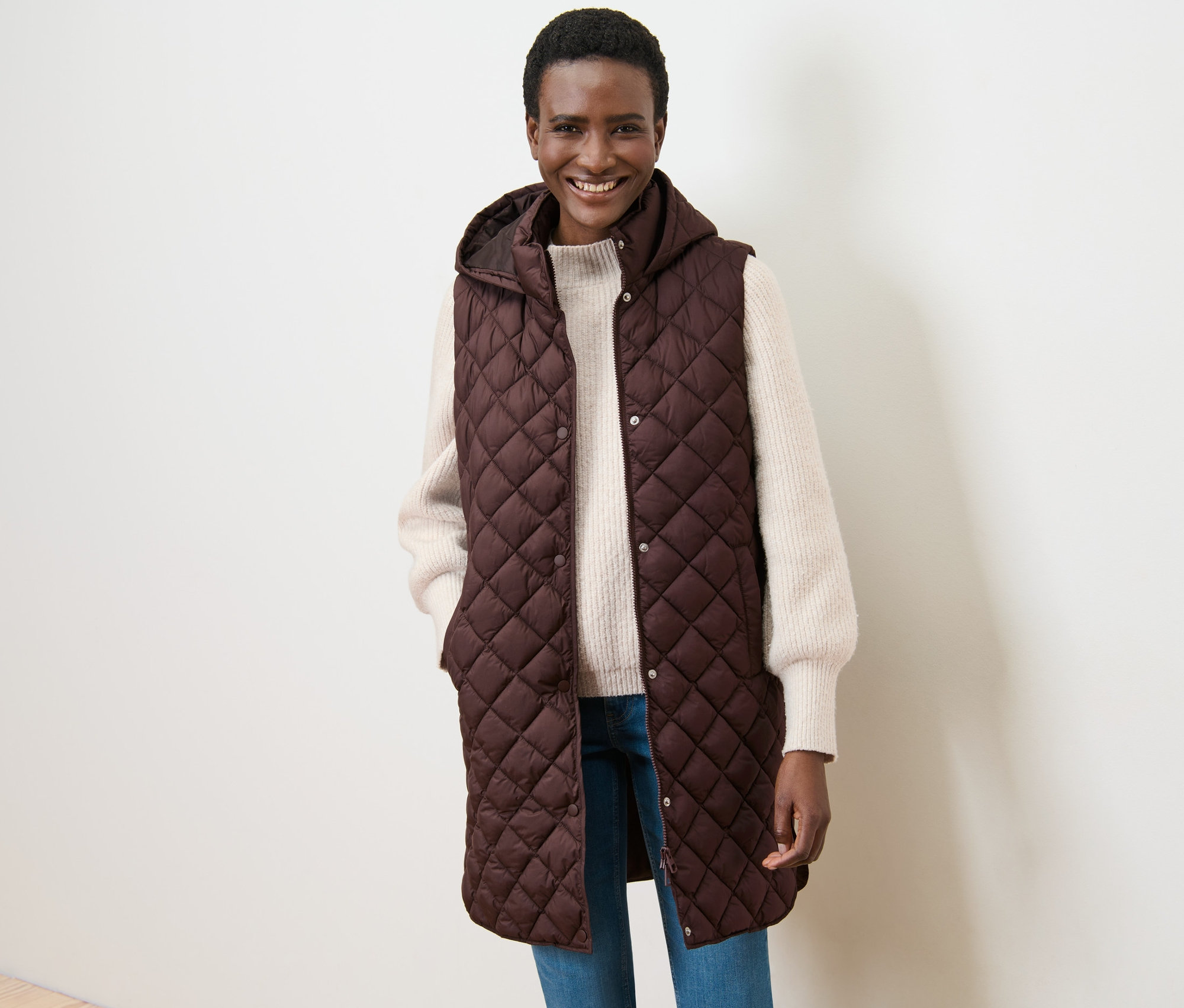 Frau lächelt und posiert in langer Steppweste mit Kapuze.