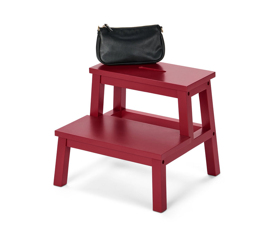 Eine schwarze Handtasche liegt auf einem roten Tritthocker.