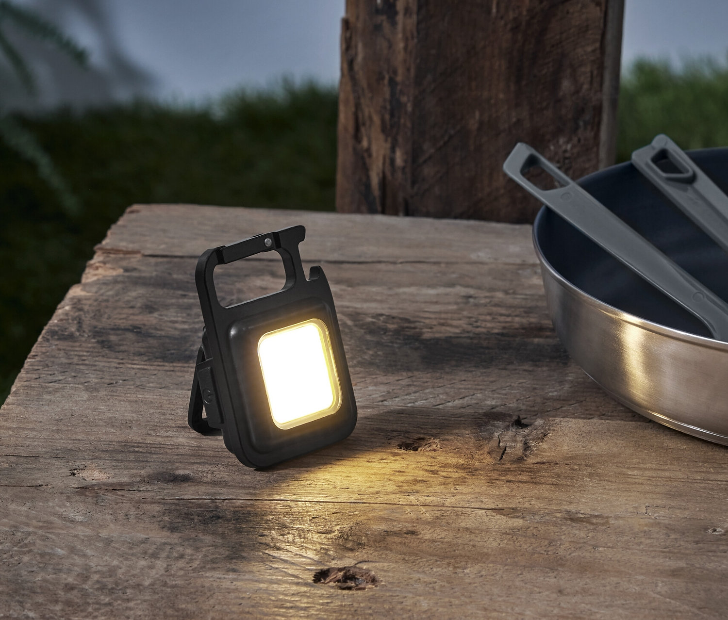 Auf einem Holztisch stehen ein Multifunktions-Licht, eine Pfanne und ein Rucksack.