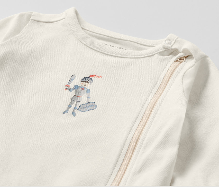 Detailansicht eines weißen Baby-Schlafanzugs mit Ritter-Motiv.