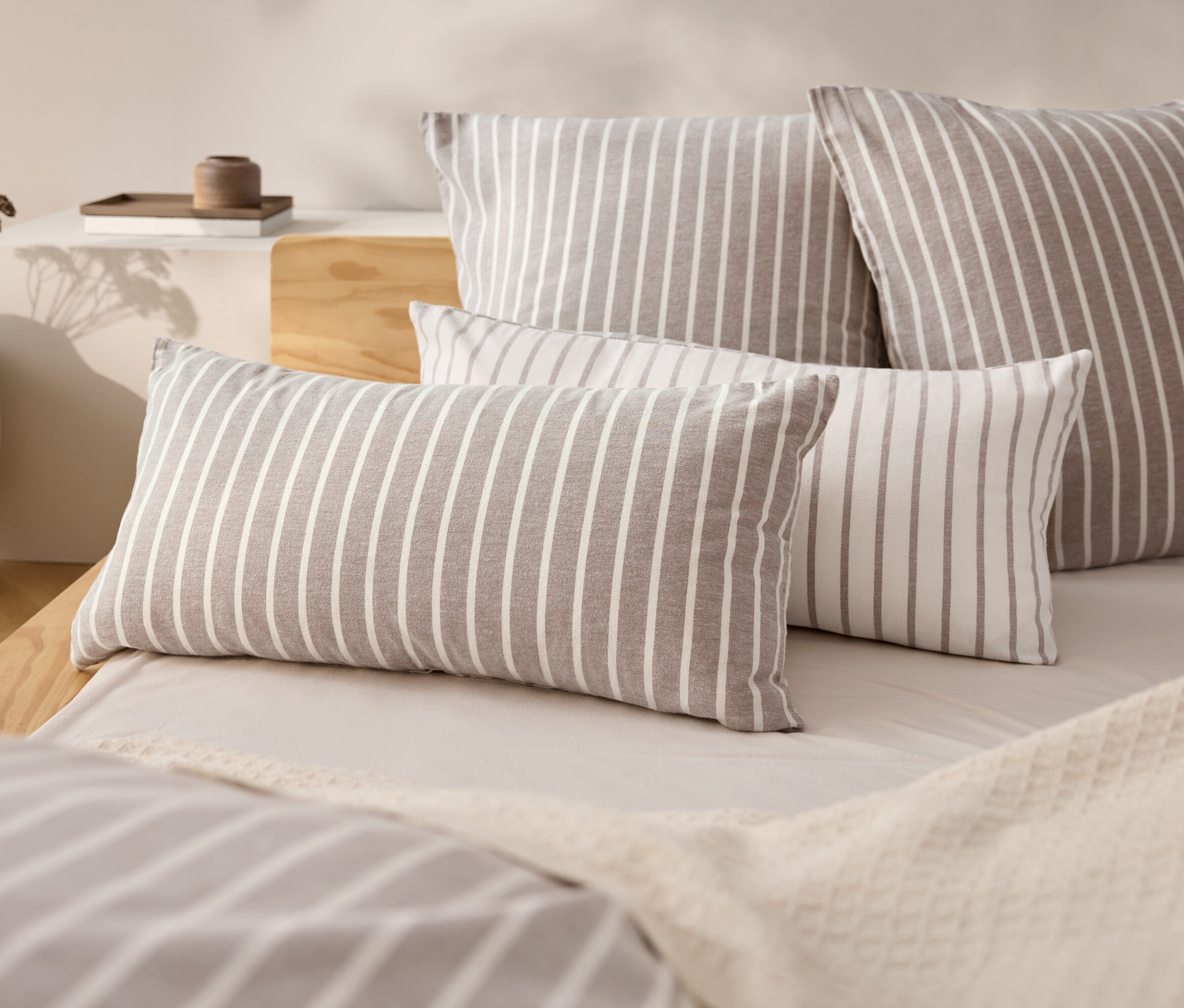 Vier gestreifte Kissen auf einem Bett mit einer beige Tagesdecke.