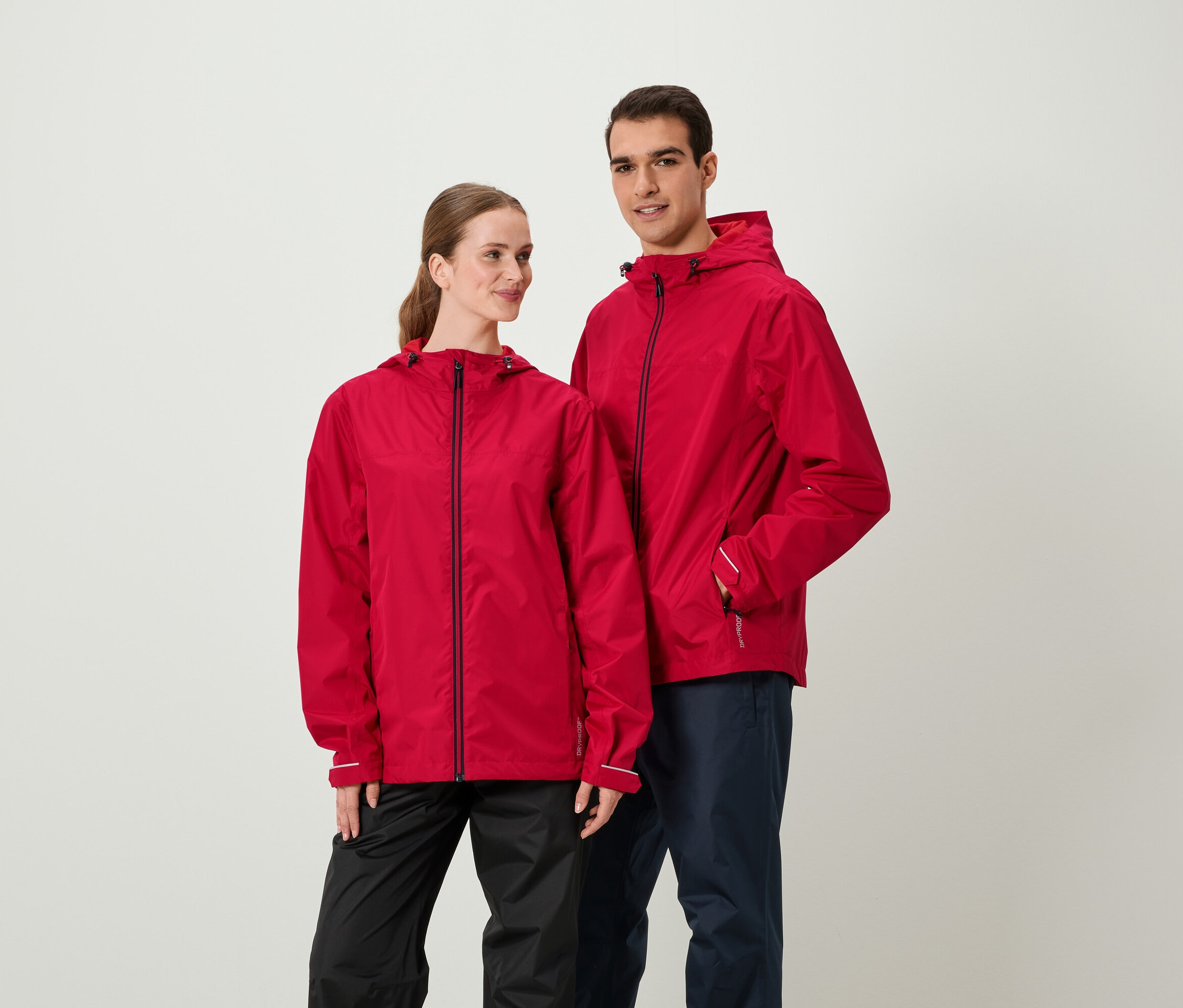 Zwei Personen in roten Jacken und dunklen Hosen stehen nebeneinander.