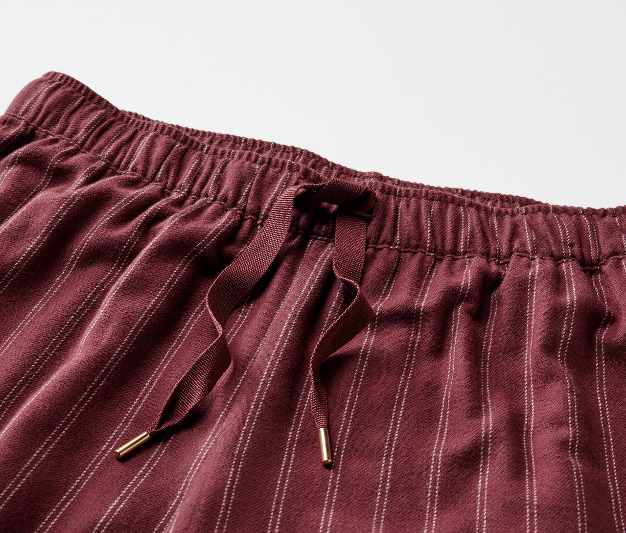 Detail einer bordeauxroten, gestreiften Hose mit Gummibund und Kordelzug.
