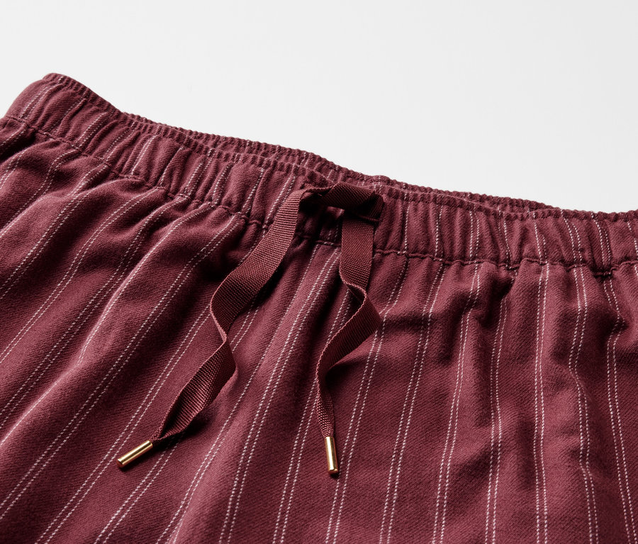 Detail einer bordeauxroten, gestreiften Hose mit Gummibund und Kordelzug.