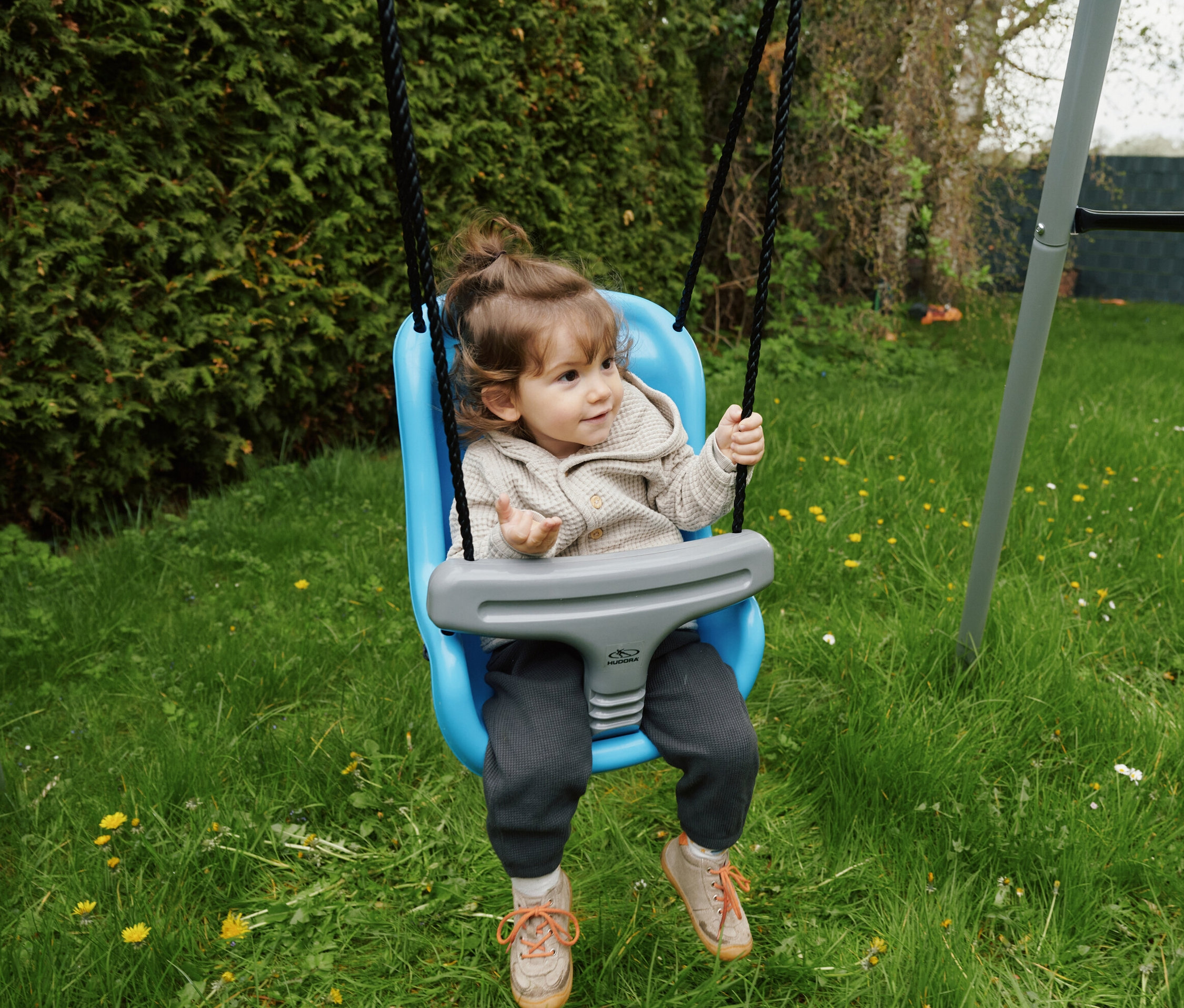 Ein Kind sitzt in einer blauen HUDORA Baby-Hochschaukel im Garten.