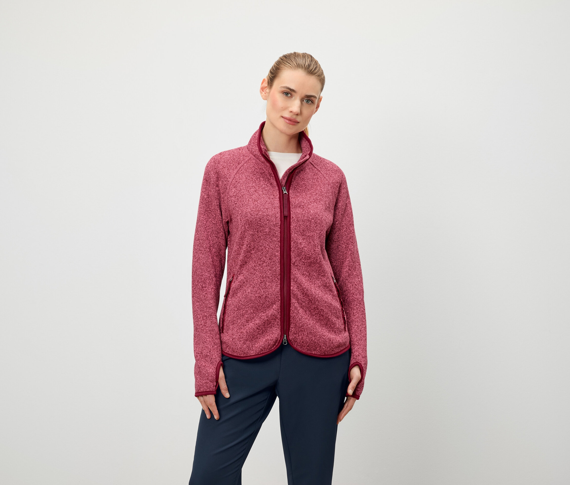 Eine Frau trägt eine langärmlige Fleecejacke mit Reißverschluss und eine dunkelblaue Hose.