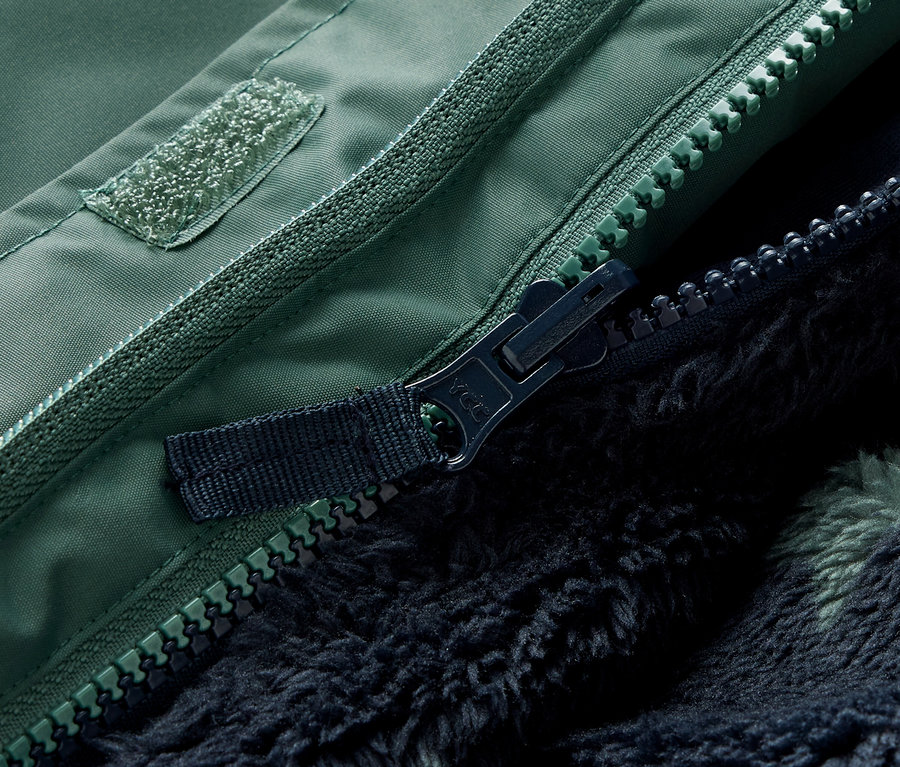Detailaufnahme vom Reißverschluss und Klettverschluss einer grünen 3-in-1-Kinderwinterjacke.