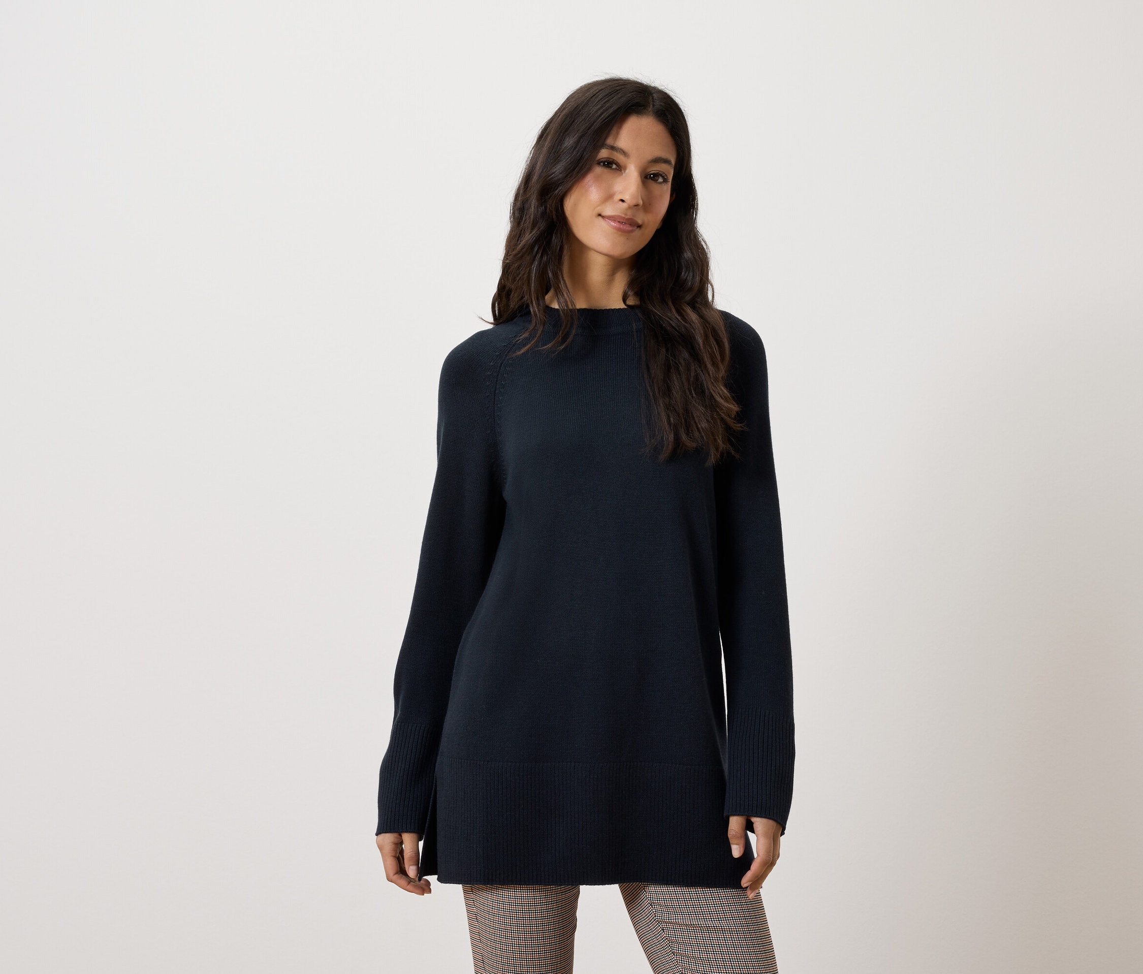 Eine Frau trägt einen langen, dunkelblauen Pullover und eine braune Hose.