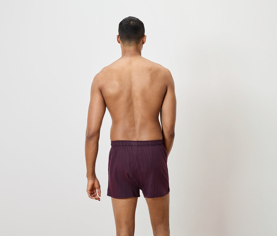 Abbildung der Rückansicht eines Mannes, der bordeauxfarbene Boxershorts trägt.
