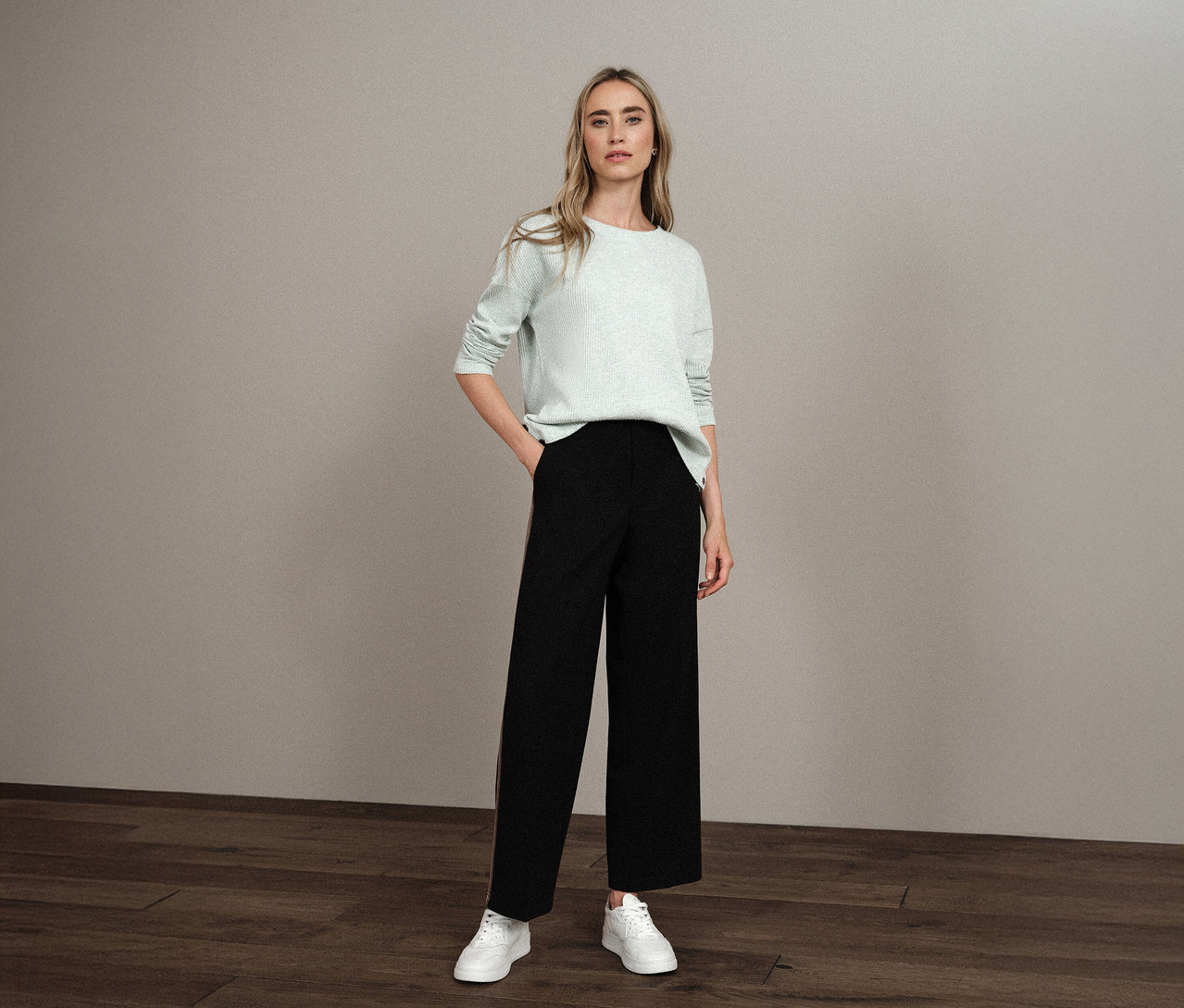 Frau steht mit der Hand in der Hosentasche und trägt ein Street One Shirt mit Struktur, eine schwarze Hose und weiße Turnschuhe.