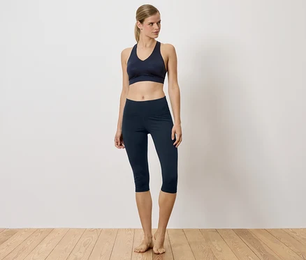 Frau in marineblauem Sport-BH und Leggings steht auf Holzboden.