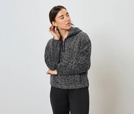 Frau posiert in grau-schwarzem Leopard-Fleece-Hoodie und schwarzer Hose.