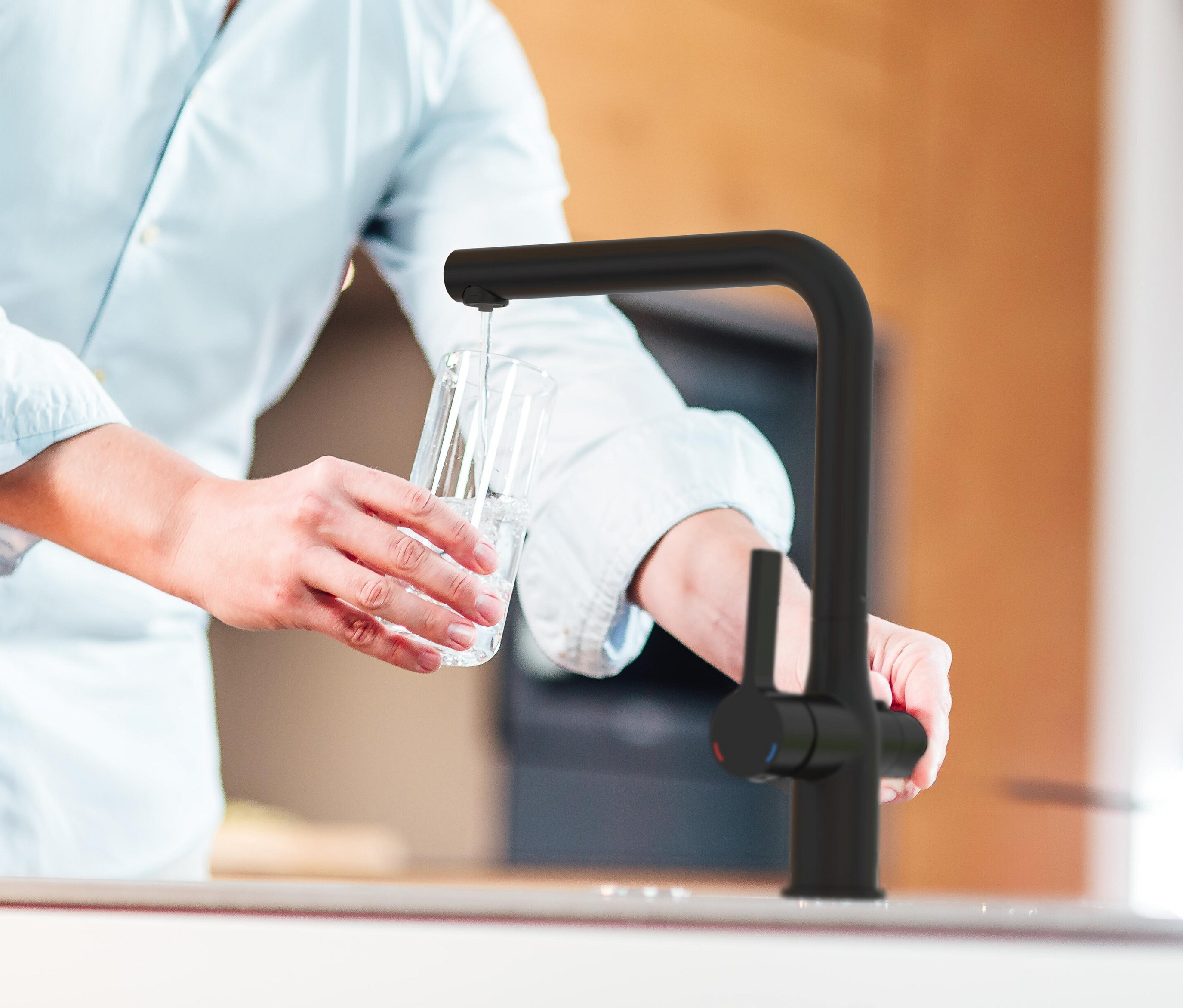 Mann füllt Wasser aus einer schwarzen Schütte AQUASTAR PRO Filterarmatur in ein Glas.