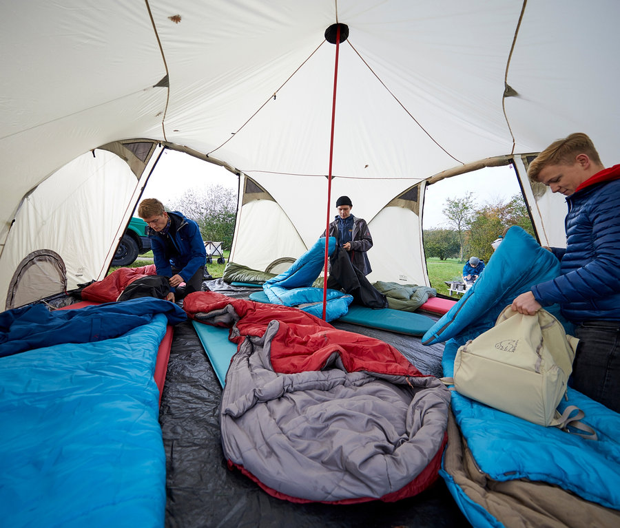 Im Zelt sind drei Personen zu sehen, die Schlafsäcke und Grand Canyon Doppel-Isomatten »Hancock 7.5« auspacken.