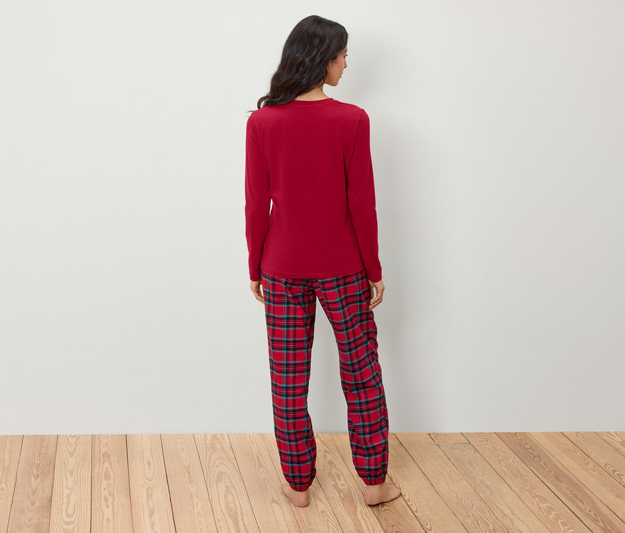 Eine Frau mit dem Rücken zur Kamera trägt einen roten Schlafanzug mit langen Ärmeln und eine karierte Hose.