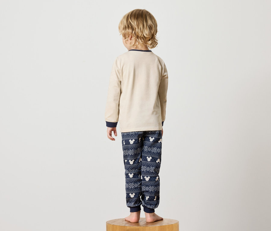 Ein Junge im Mickey-Mouse-Pyjama steht mit dem Rücken zur Kamera auf einem Holzsockel.