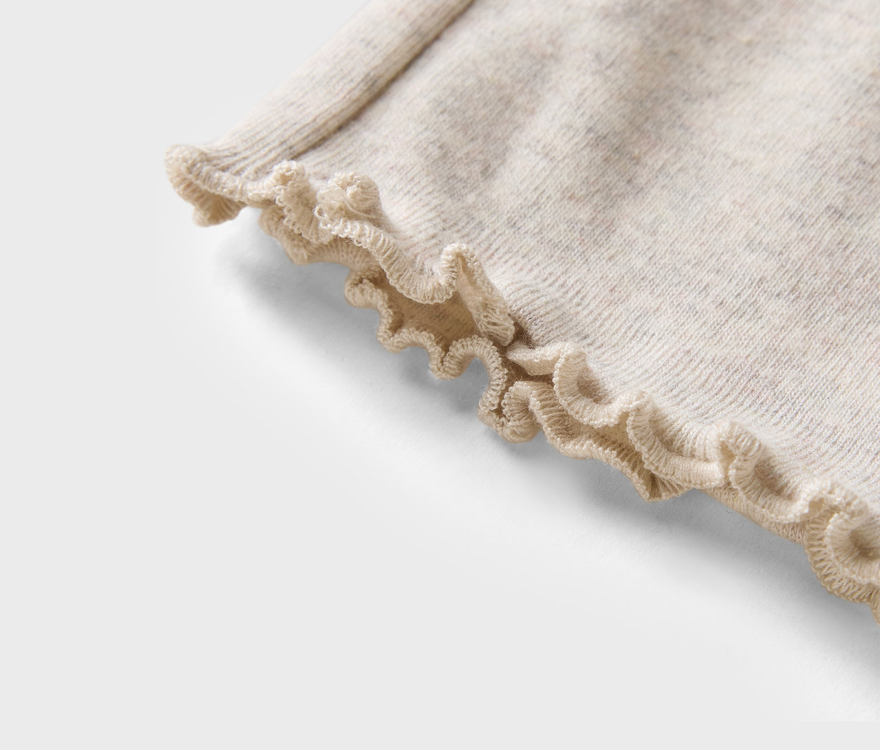 Detail eines beigen Pullovers mit Rüschensaum.