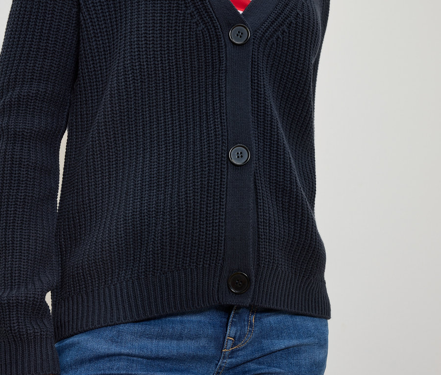 Torso einer Person in marineblauer Strickjacke mit Knöpfen und blauen Jeans.