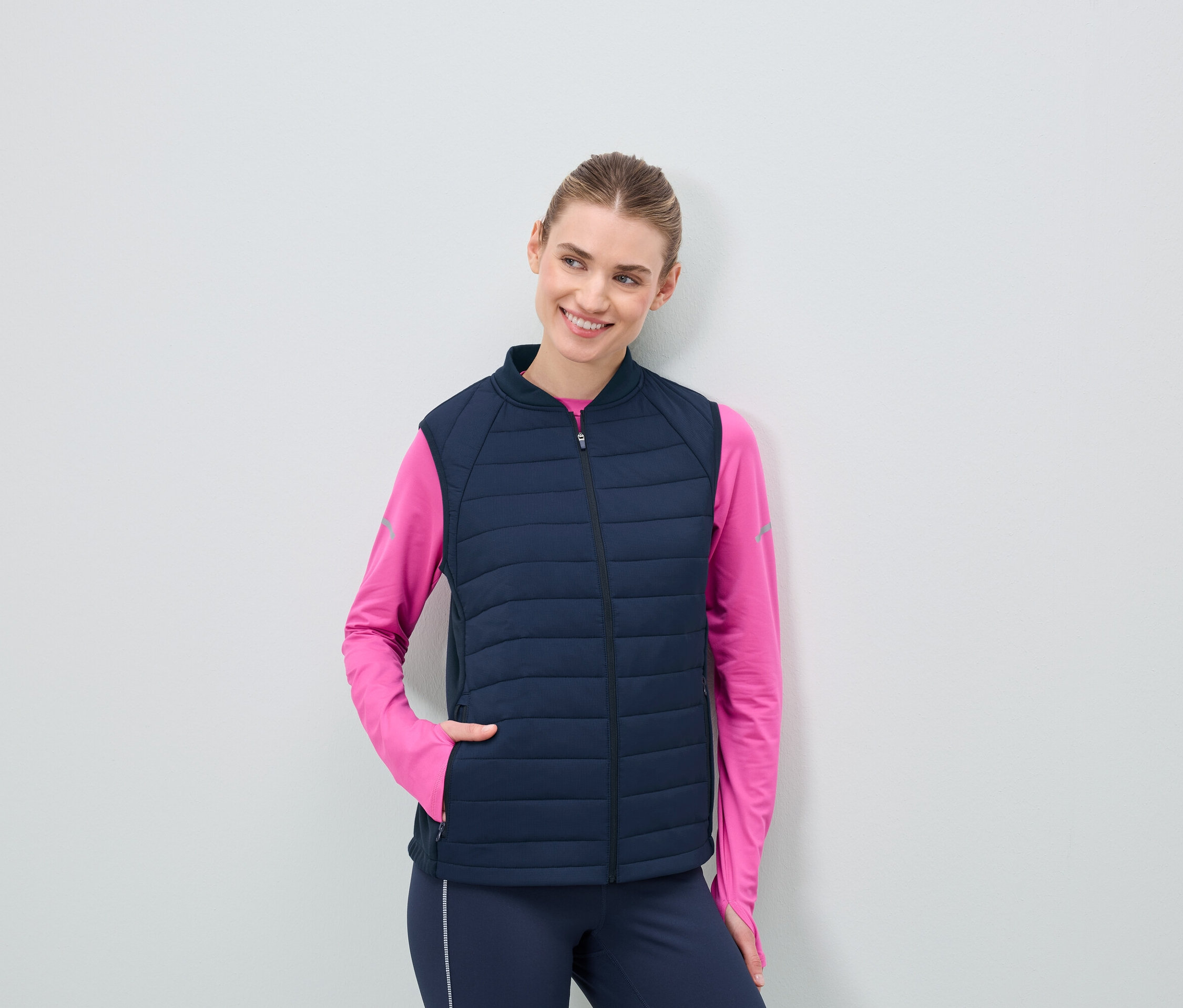 Frau trägt eine dunkelblaue Steppweste und ein pinkes Langarmshirt.