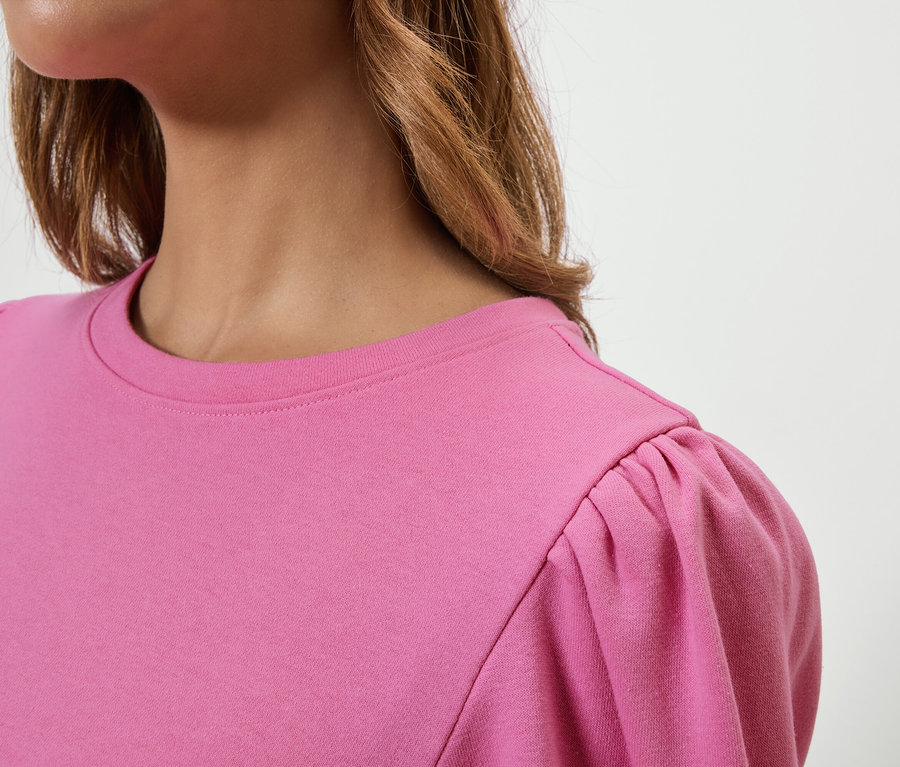 Oberkörper einer Frau in einem rosafarbenen T-Shirt mit gerafften kurzen Ärmeln.