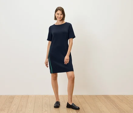 Eine Frau steht und trägt ein dunkelblaues Kleid mit kurzen Ärmeln und einem grünen Streifen an der Seite.