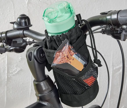 Eine Fahrrad-Snacktasche ist am Lenker eines Fahrrads befestigt, die eine Wasserflasche und einen Müsliriegel enthält.