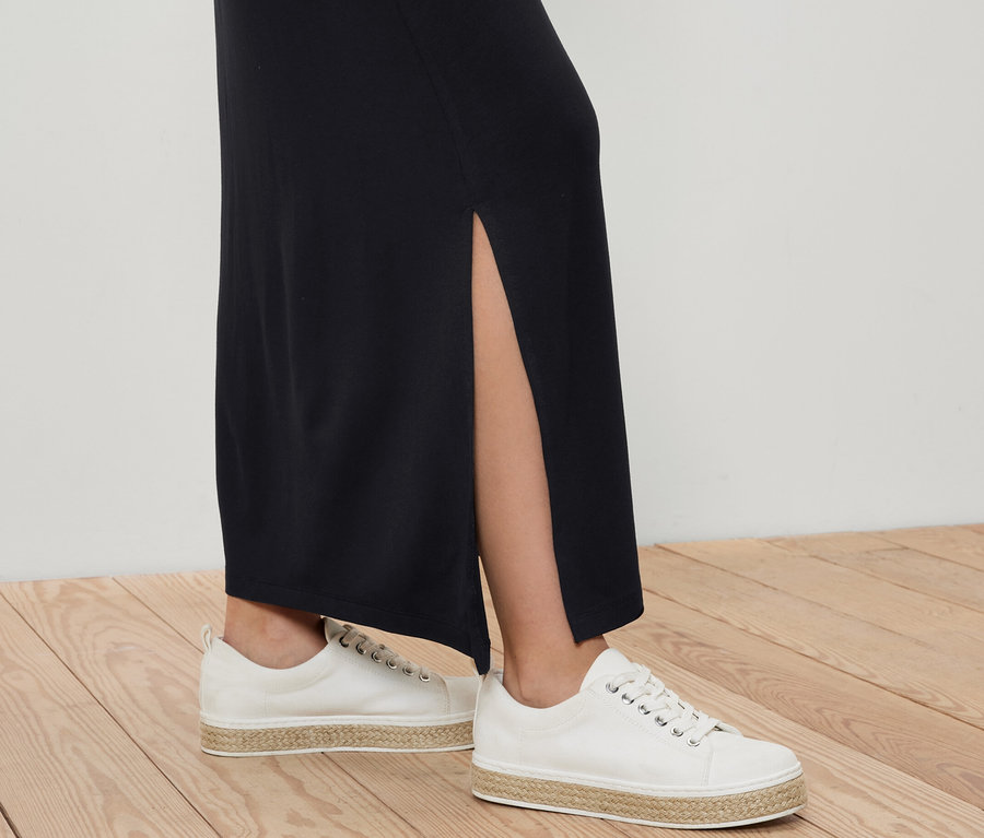 Beine einer Frau in langem Jerseyrock und weißen Leinenschuhen auf Holzboden.