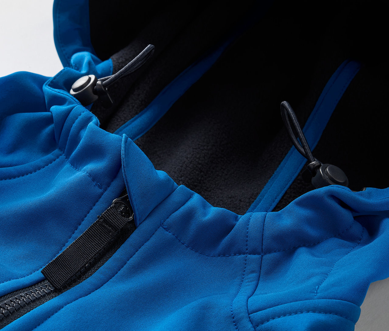 Detailaufnahme einer blauen Softshelljacke mit Reißverschluss und Kapuze.