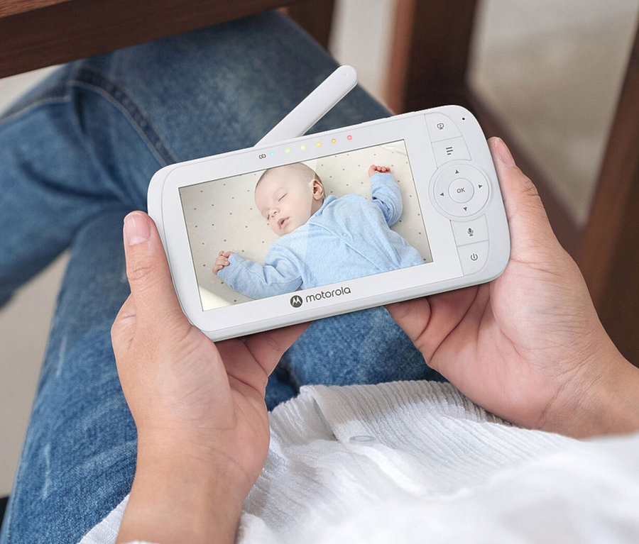Frau hält ein weißes Video-Babyphone »VM34« in der Hand, auf dessen Bildschirm ein Baby schläft.