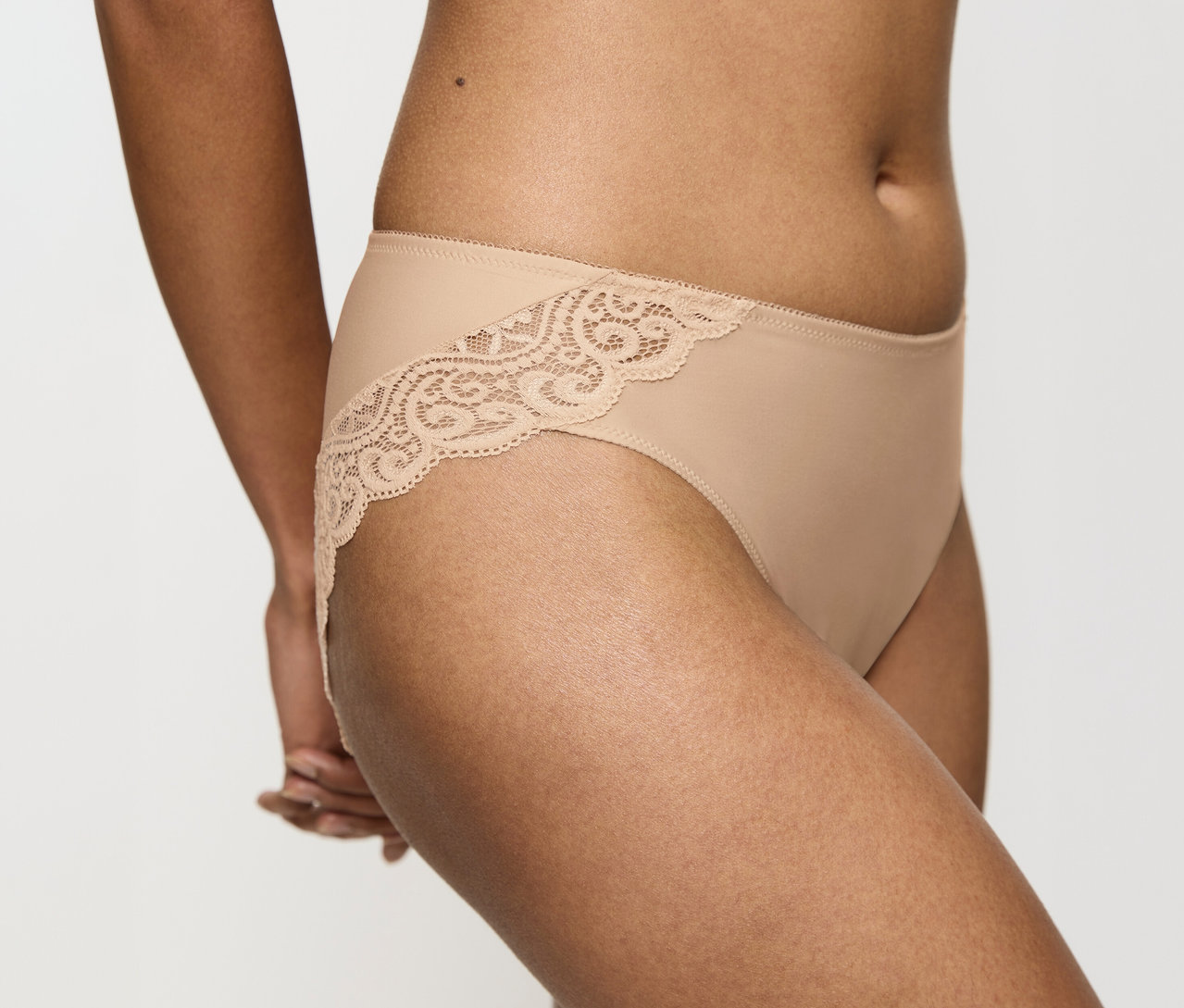 Eine Person trägt einen hautfarbenen Triumph Amourette Tai Slip mit Spitzenbesatz an den Seiten.