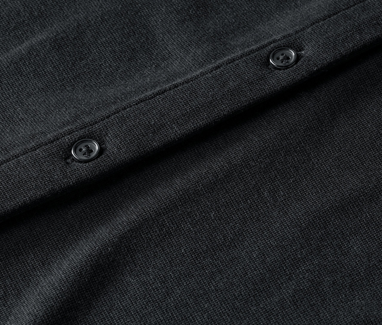 Detailansicht einer schwarzen Strickjacke mit Knöpfen.