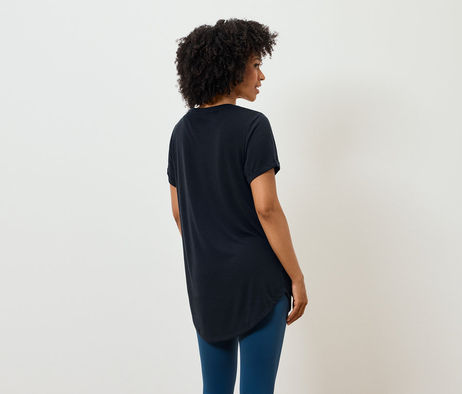 Frau mit Afro-Frisur steht mit dem Rücken zur Kamera und trägt ein schwarzes T-Shirt und blaue Leggings.