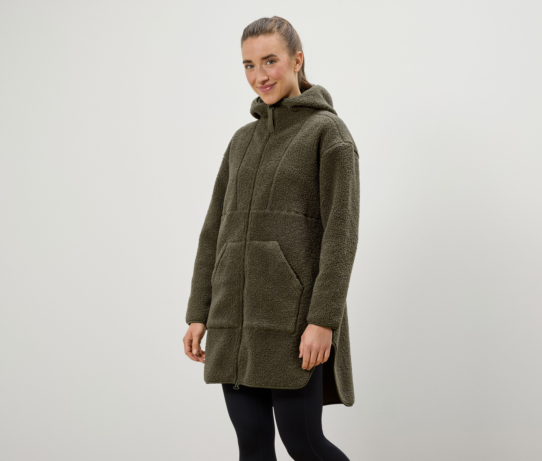 Frau trägt einen olivgrünen Kapuzenmantel und schwarze Leggings.