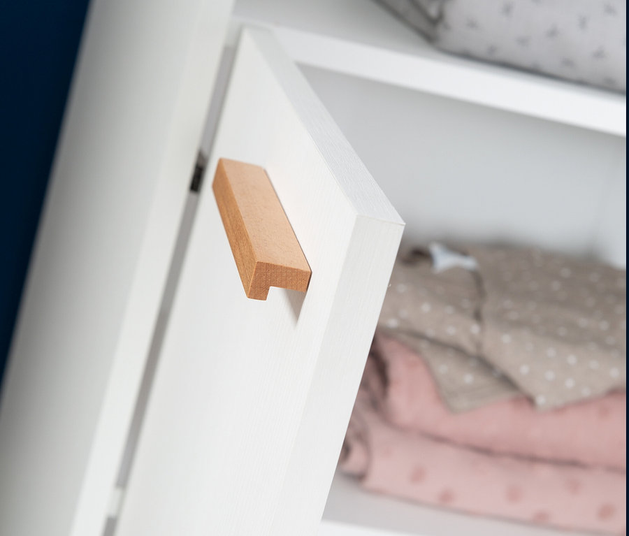 Detail einer weißen roba Wickelkommode »Anton« mit Holzgriff und teilweise geöffneter Tür, im Inneren sind gefaltete Kleidungsstücke zu sehen.
