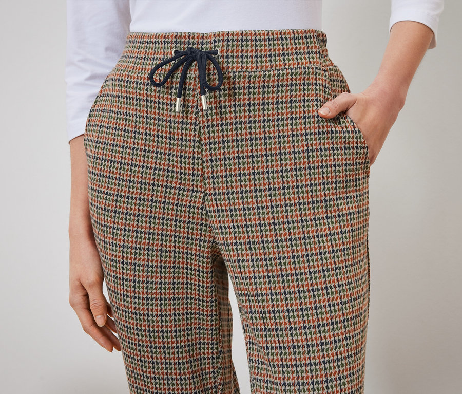 Detail einer Damenhose mit Hahnentrittmuster, eine Hand in der Hosentasche.