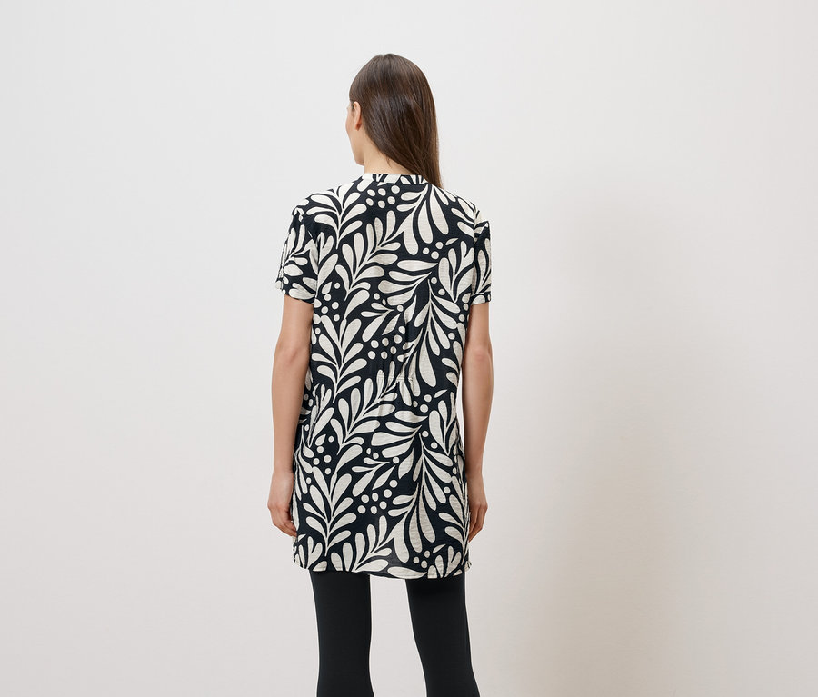 Rückansicht einer Frau mit langen braunen Haaren, die ein kurzärmeliges, schwarz-weißes Kleid mit Blattmuster und schwarze Leggings trägt.