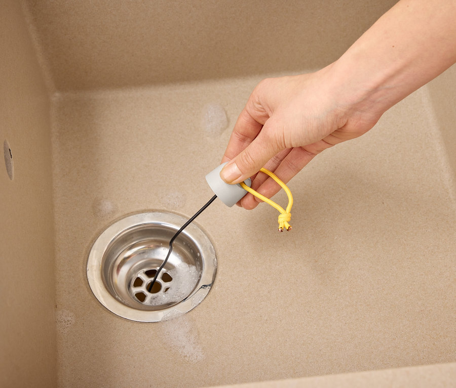 Hand führt Abflussreiniger in Spüle mit Wasser.