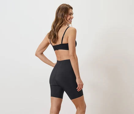 Eine Frau steht mit dem Rücken zur Kamera und trägt einen schwarzen BH und Shorts.