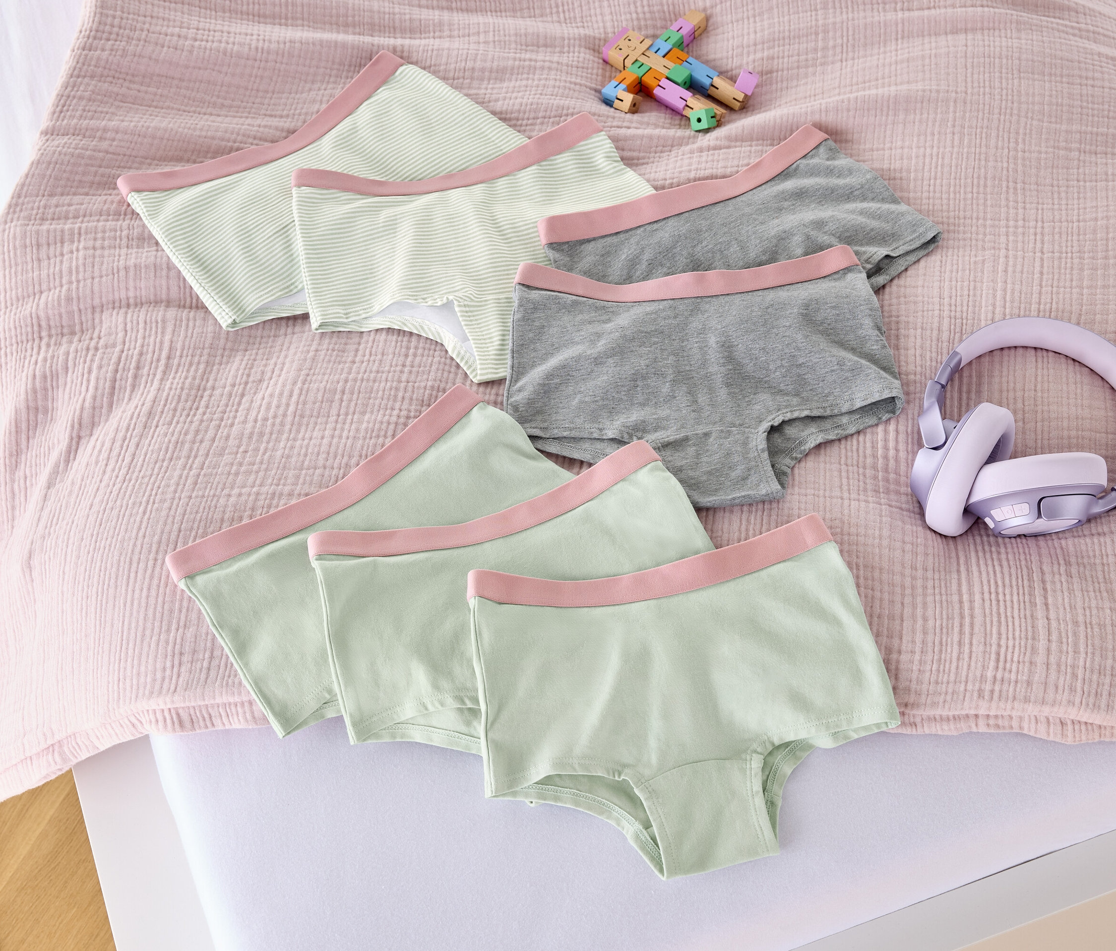 Auf einem Bett liegen sieben altrosa Mädchen-Pantys, ein Spielzeug und Kopfhörer.