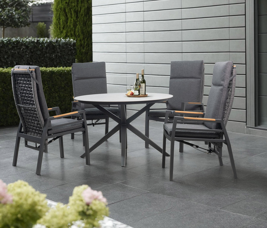 Ein hellgrauer deVries Tisch (Ø ca. 120 cm) mit vier Stühlen steht auf einer Terrasse.