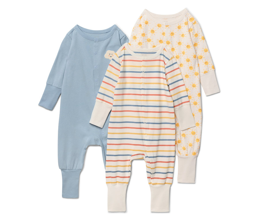 Drei Baby-Schlafanzüge liegen auf einem weißen Hintergrund. Der linke Schlafanzug ist blau mit einer kleinen Wolke auf der Brust. Der mittlere Schlafanzug ist gestreift in den Farben Beige, Gelb, Rot und Blau. Der rechte Schlafanzug ist cremefarben mit einem gelben Sonnenmuster.