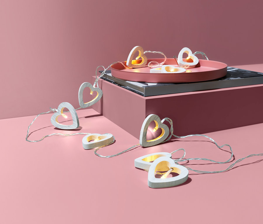 LED-Lichterkette mit Holzherzen auf rosa Hintergrund.