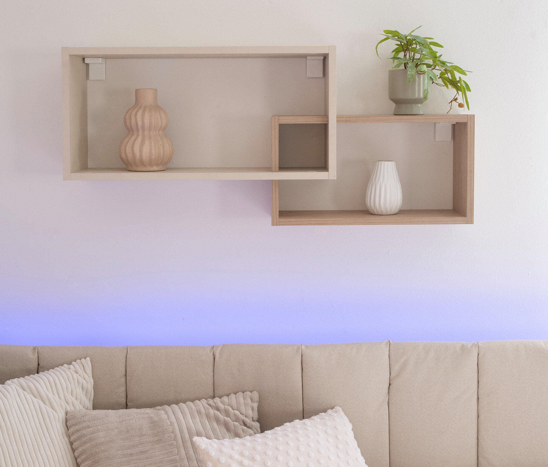 An der Wand hängt ein Roba Wandregal »Louisa« mit einer Vase und einer Pflanze. Darunter befindet sich ein beiges Sofa mit Kissen.