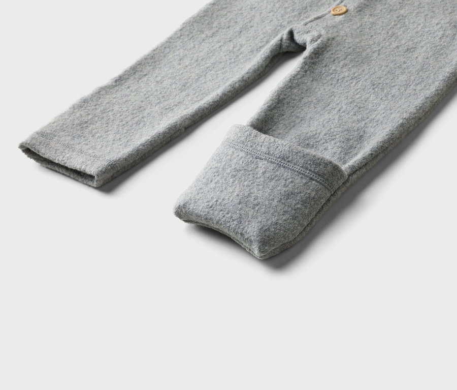 Nahaufnahme eines grauen Baby-Overalls mit langen Ärmeln und umgeschlagenen Bündchen vor einem neutralen Hintergrund.