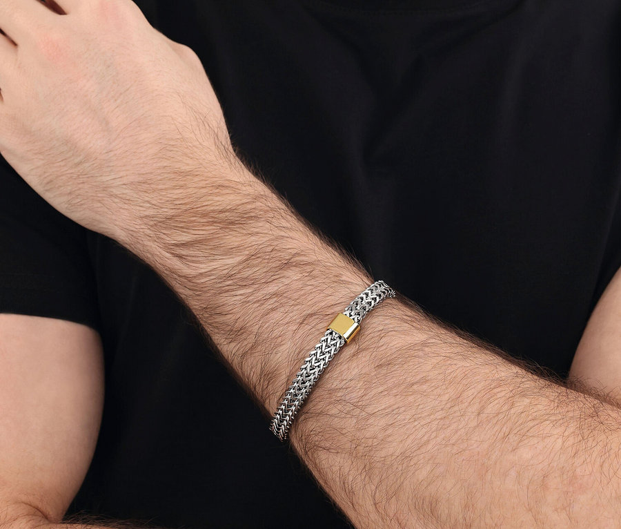 Nahaufnahme eines Mannes mit einem silbernen Armband mit goldenem Verschluss am Handgelenk, während er ein schwarzes T-Shirt trägt.