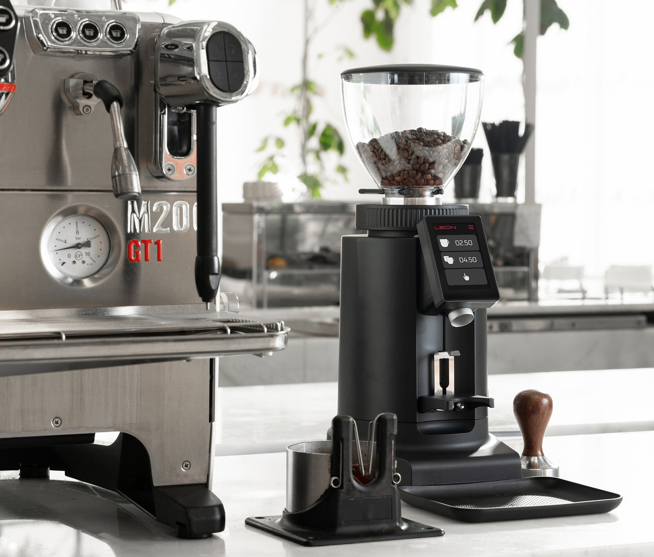 Nahaufnahme einer silbernen Espressomaschine neben einer schwarzen Kaffeemühle auf einer weißen Theke.