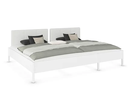 Weißes Doppelbett mit zwei Matratzen, grauen Decken und Kissen.