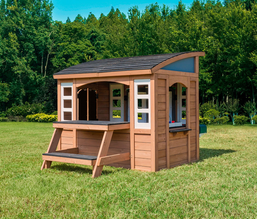 Das Spielhaus Trolli steht auf einer Wiese vor Bäumen. Das Spielhaus hat eine kleine Veranda mit einer Bank.