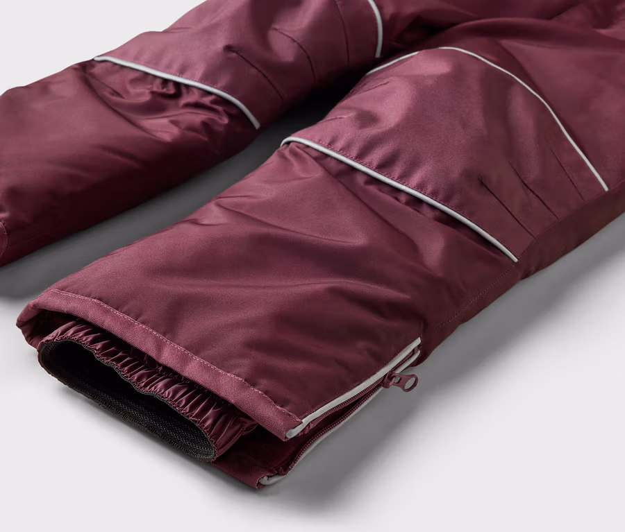 Nahaufnahme einer burgunderroten Hose mit weißer Paspelierung und Reißverschluss am Beinabschluss.